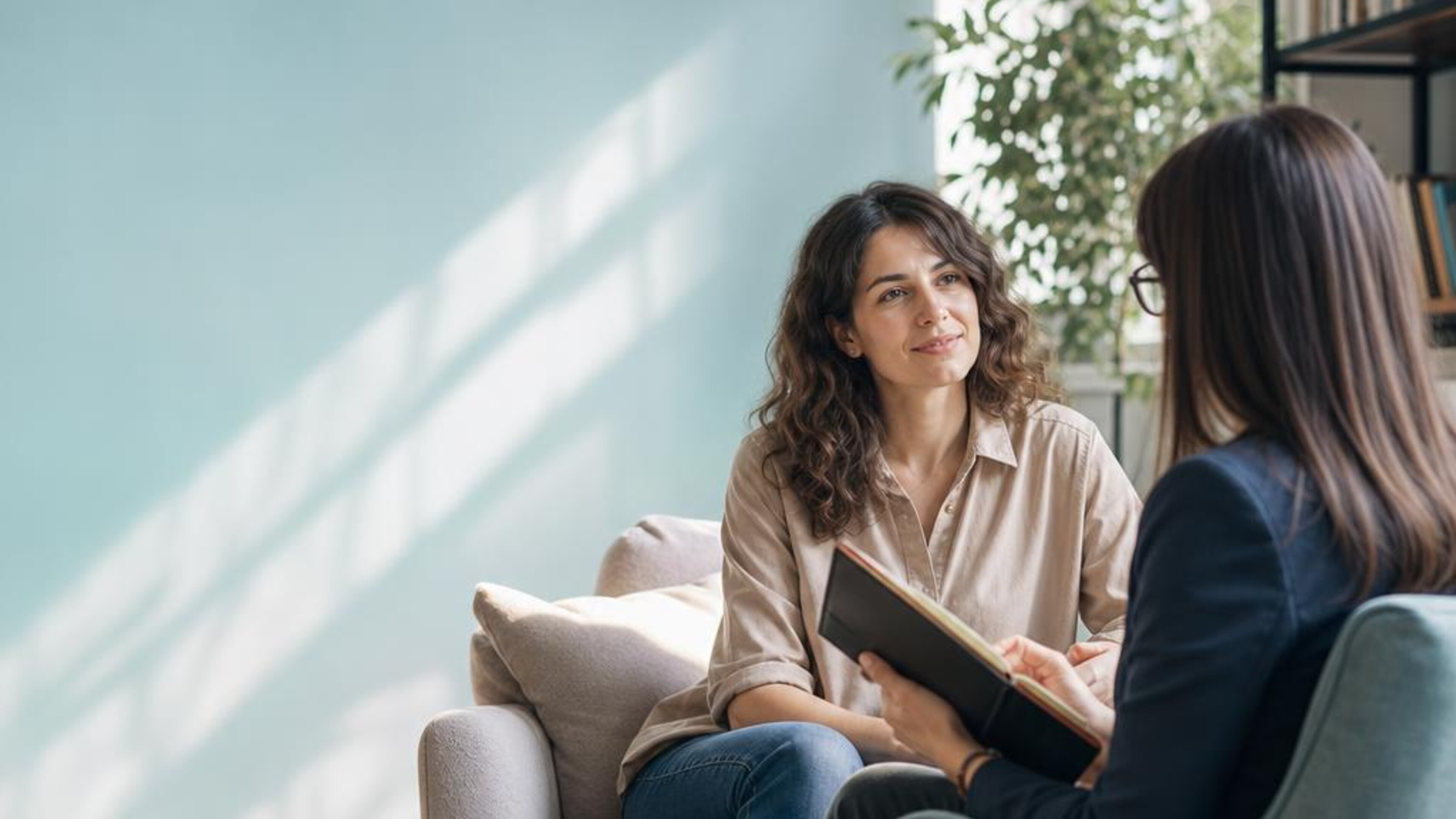 An adult and therapist having a calm conversation beside a sunlit window, illustrating OCD support. Generated illustration, not actual patients or clinic staff.